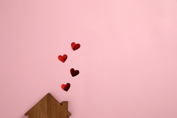 Figure of wooden house and red hearts as smoke from chimney on pink background, flat lay. Space for...