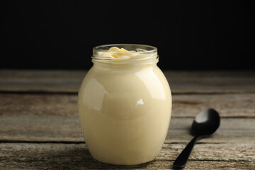 Jar of delicious mayonnaise and spoon on wooden table