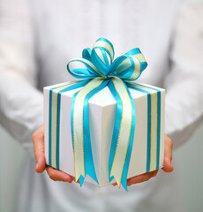 Close up shot of female hands holding a big gift box wrapped with blue ribbon.