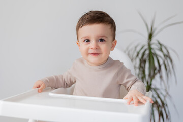 cheerful smiling baby is sitting in a white high chair for feeding. white background