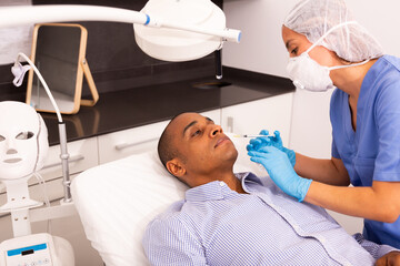 Portrait of Hispanic male client of aesthetic cosmetology clinic during procedure of face...