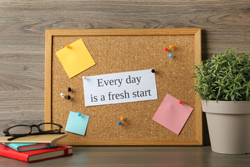 Cork board with motivational quote Every Day is a Fresh Start, stationery and plant on wooden table