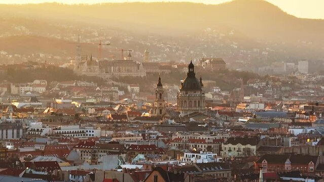 Beautiful sunlight over the Hungarian populous inner city with the St Setphen's Basilica of the sunset behind the high green hills of the city of Budapest. Wide drone lifting shot
