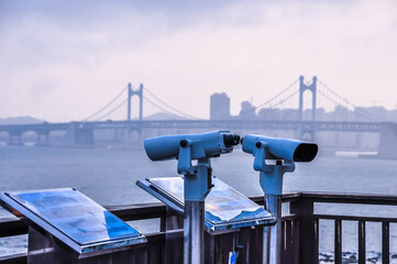 Coin-operated binoculars. Binocular telescope on the observation deck for tourism. Spyglass or telescope pointing towards the sea, city background. A telescope on the other side of the river. 