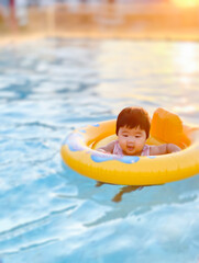 Happy cute little baby child learning to swim with swimming ring in an indoor pool. Smiling little child, newborn girl having fun. Active family spending leisure and time in spa hotel.