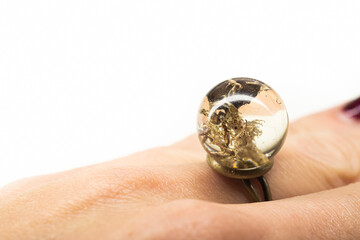 Natural moss preserved resin ring. Clear transparent plastic sphere ball on a female finger. Bronze base. Selective focus on the details, blurred background.