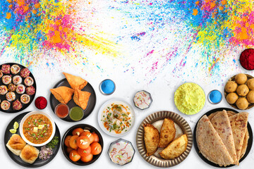 Assorted Indian Holi festival food like samosa, kachori, Puri bhaji, Pav Bhaji, Laddo, Sweets, Dahi vada, puranpoli, gujiya, gulab jamun with colorful background and colors with copy space.