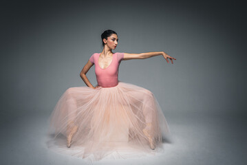 Naklejka premium young pretty, fragile, beautiful ballerina dancing in a long pale pink dress with tulle on a uniform background, hand movements, restrained tone. Ballet, dance, dancer. Place for inscription