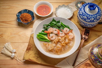 Wide Rice Noodles with Shrimp and kale in Gravy Sauce  Served with condiments, chili powder , chili sauce and sugar. Asian food.