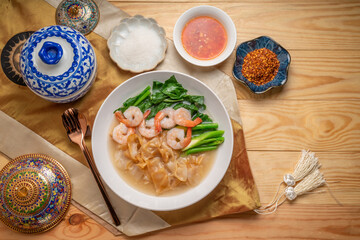Wide Rice Noodles with Shrimp and kale in Gravy Sauce  Served with condiments, chili powder , chili sauce and sugar. Asian food.