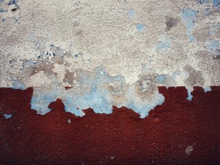 surface of the old cement wall, painted white and dark red, has cracks.