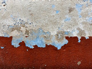 surface of the old cement wall, painted white and dark red, has cracks.
