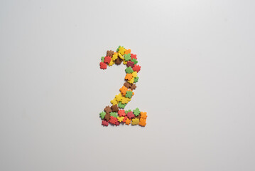 Numeral two from sweet pastry topping in the form of colorful foliage on a white background.