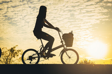 Fototapeta premium Silhouette of woman ride a bicycle along the bike lane in the park at the sunset.