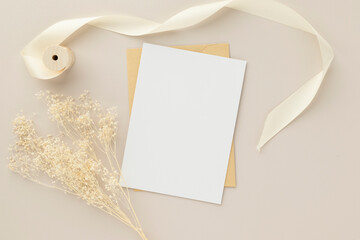 Blank greeting card invitation Mockup 5x7 on Brown envelope with dried flowers on beige background, flat lay, mockup