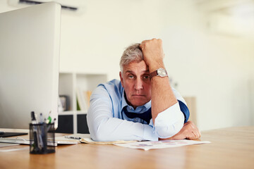 Fototapeta premium When is this day going to end. Portrait of a mature businessman looking stressed out while sitting at his desk in an office.