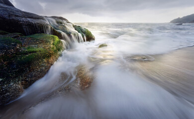 Beautiful long exposure shot of seascape at sunrise,silky smooth sea wave sweeping past the rock.