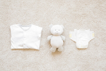 Fototapeta na wymiar White folded newborn bodysuit, diaper and teddy bear on light blanket background. Closeup. Baby things. Top down view.