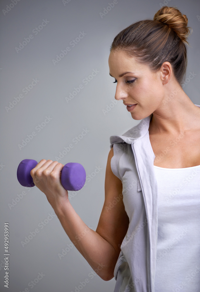 Wall mural Strengthening her biceps. A young woman working out with weights.