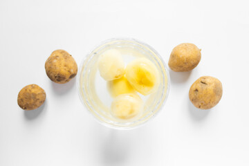 Top view of glass bowl with water and peeled potatoes and raw unpeeled potato vegetables. White background.