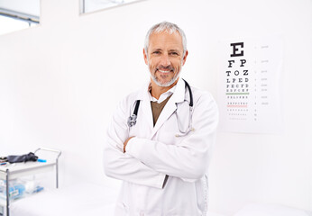 Lets find the perfect pair of glasses for you. Portrait of a mature male optometrist standing in his office with an eye chart in the background. - obrazy, fototapety, plakaty