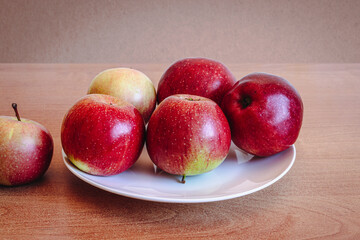 Red apples on a white plate on a wooden table. Selective focus.