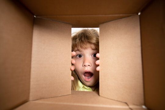 Kid opening package. Child boy age 6 year opening a carton box and looking inside, unpacking concept, surprise unboxing.
