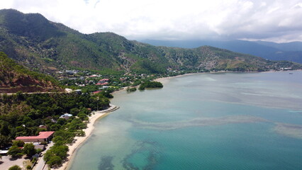The white sandy beach coastline and green hills, aerial drone view of landscape and blue ocean, in Dili, Timor Leste, Southeast Asia