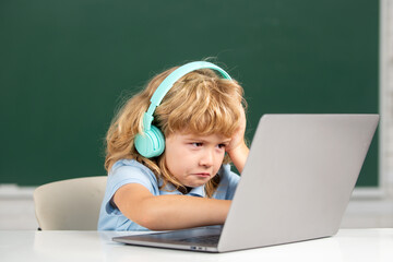 Angry sad child boy in headphones using a laptop and study online with video call teacher at...