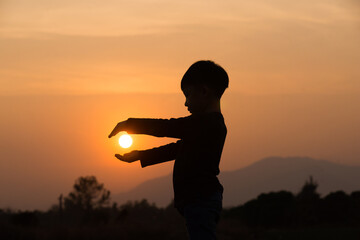 A boy playing with the sun at sunset. Silhouette picture with orange sunset sky. 