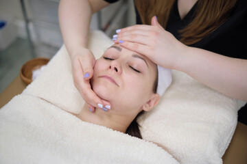 Fototapeta na wymiar Woman receiving head massage. Calm patient woman undergoing the cosmetic facial massage procedures for rejuvenation skin face
