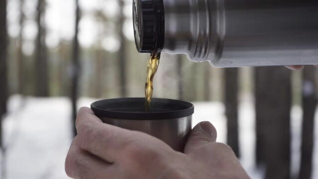 Slow motion: Close-up of a man pouring hot tea from a thermos into a mug outdoors in the cold weather