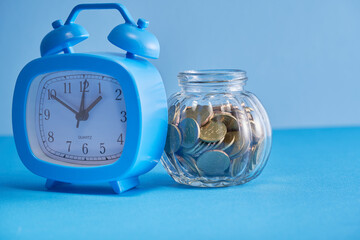 savings jar and alarm clock against blue background