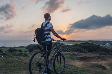 Fototapeta premium Young man stands with his bicycle in the evening and admires nature