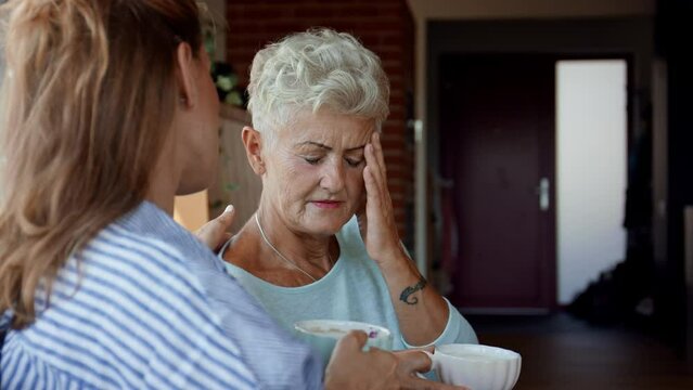 Adult daughter consoling unhappy senior mother and supporting her in struggle indoors at home.