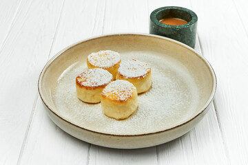 Syrniki with sweet sauce in a plate on a white wooden background