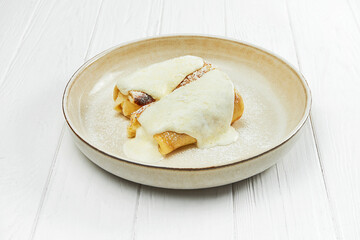 Crepes with sweet filling and sour cream in a plate on a white wooden background