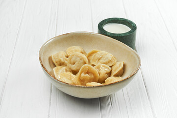 Dumplings with meat in a plate with sour cream on a white wooden background