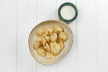 Dumplings with meat in a plate with sour cream on a white wooden background
