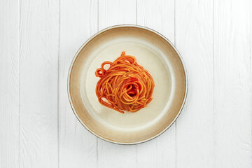 Spaghetti with red tomato sauce in a plate on a white wooden background