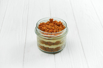 Sponge cake with cream in a jar on a white wooden background