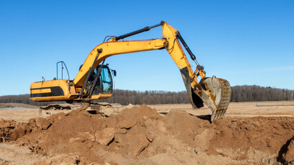 Fototapeta na wymiar A powerful caterpillar excavator digs the ground against the blue sky. Earthworks with heavy equipment at the construction site.