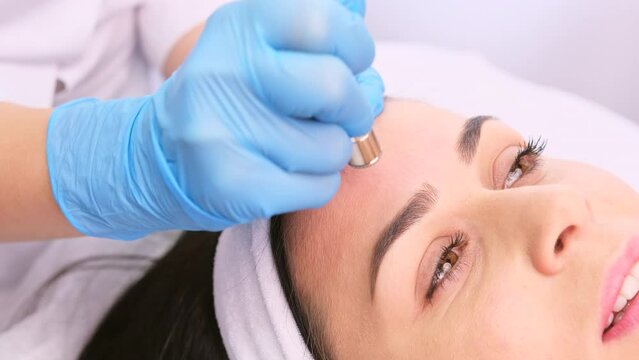 Professional beautician in blue gloves making microdermabrasion procedure of cleaning face with vacuum blackhead remover.