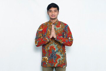 portrait of young javanese man wearing batik showing welcome hand gesture isolated on white background
