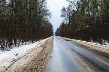 Fototapeta premium Dirty roadside in the winter period from reagents. A winter road goes into the distance through a mixed forest on a winter day