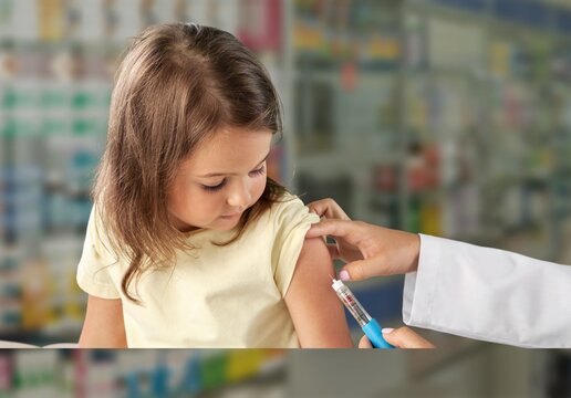 Female Nurse Giving An Arm Injection To A Child. Little Kid In Getting A Shot At A Modern Vaccination Center. Covid 19 Vaccine To A Little Girl