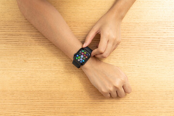 Female hands touching on a smart watch on wooden desk , top view.