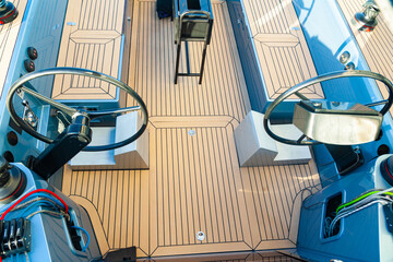 Deck of a sailing yacht with two steering wheels, sail winches, ropes with stoppers, gear lever.