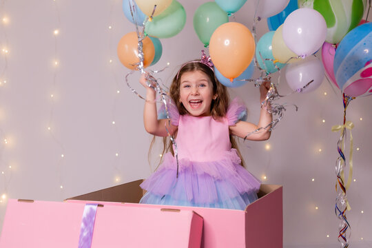 beautiful little girl with balloons jumps out of a huge pink box. child celebrates his birthday
