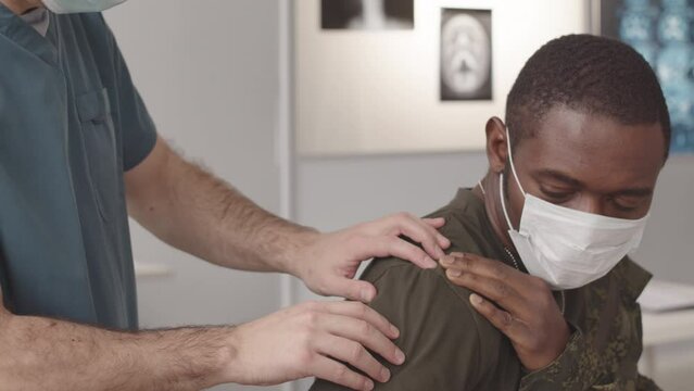 Medium closeup with slowmo of African American soldier with shoulder dislocation being examined by army doctor